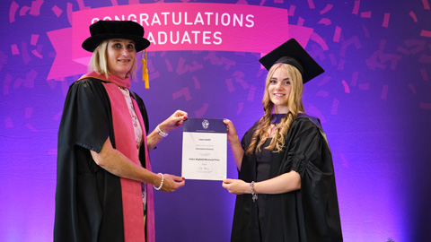 Two people in graduation attire; one hands a certificate to the other